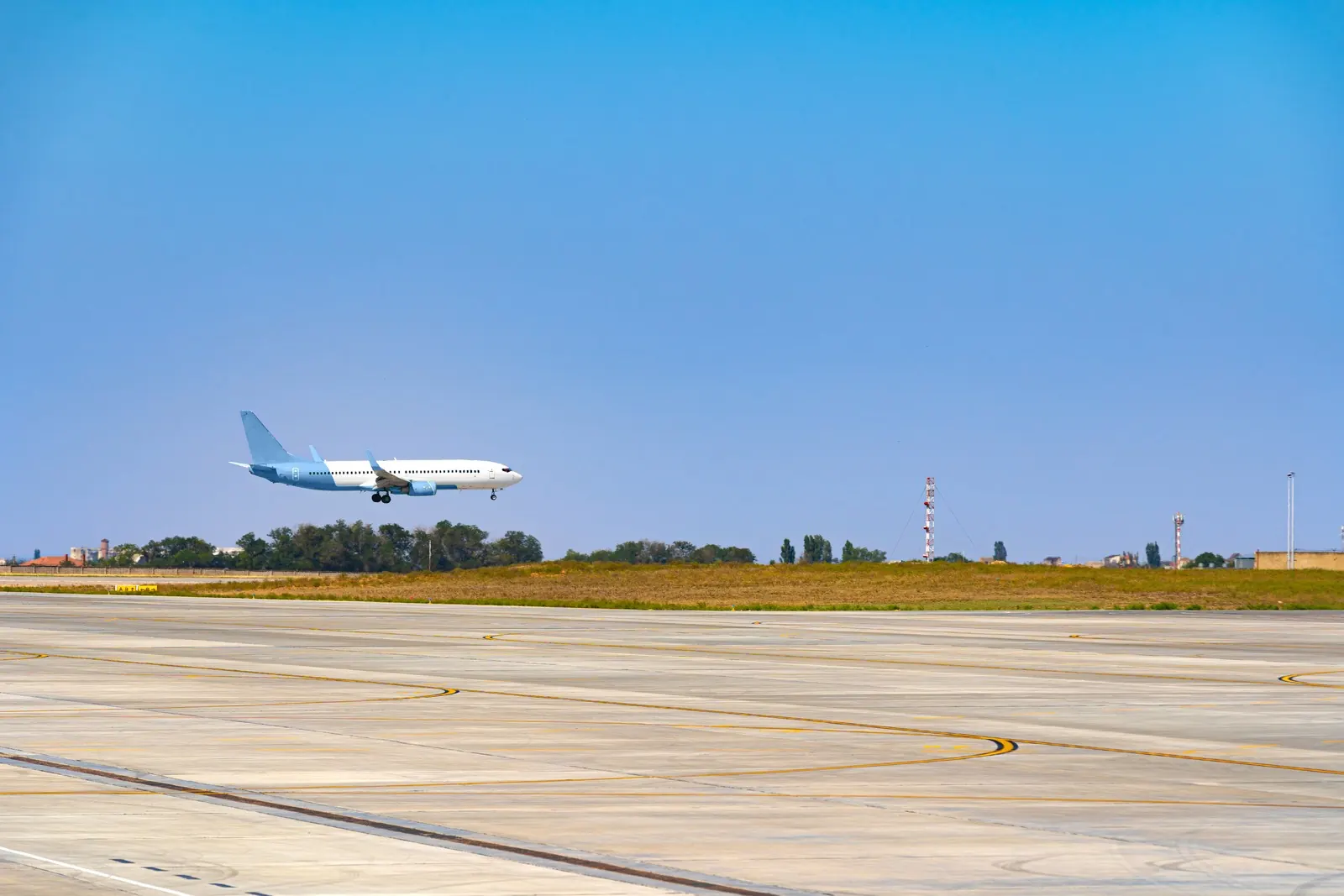 A passenger plane flying low over a grassy airfield.
