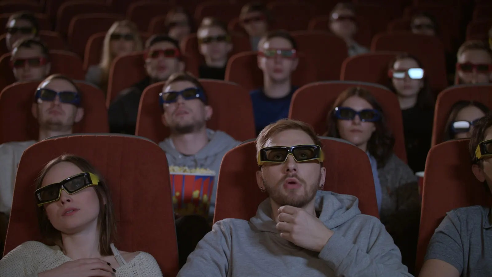 A crowd in a cinema watches a film through 3D glasses.