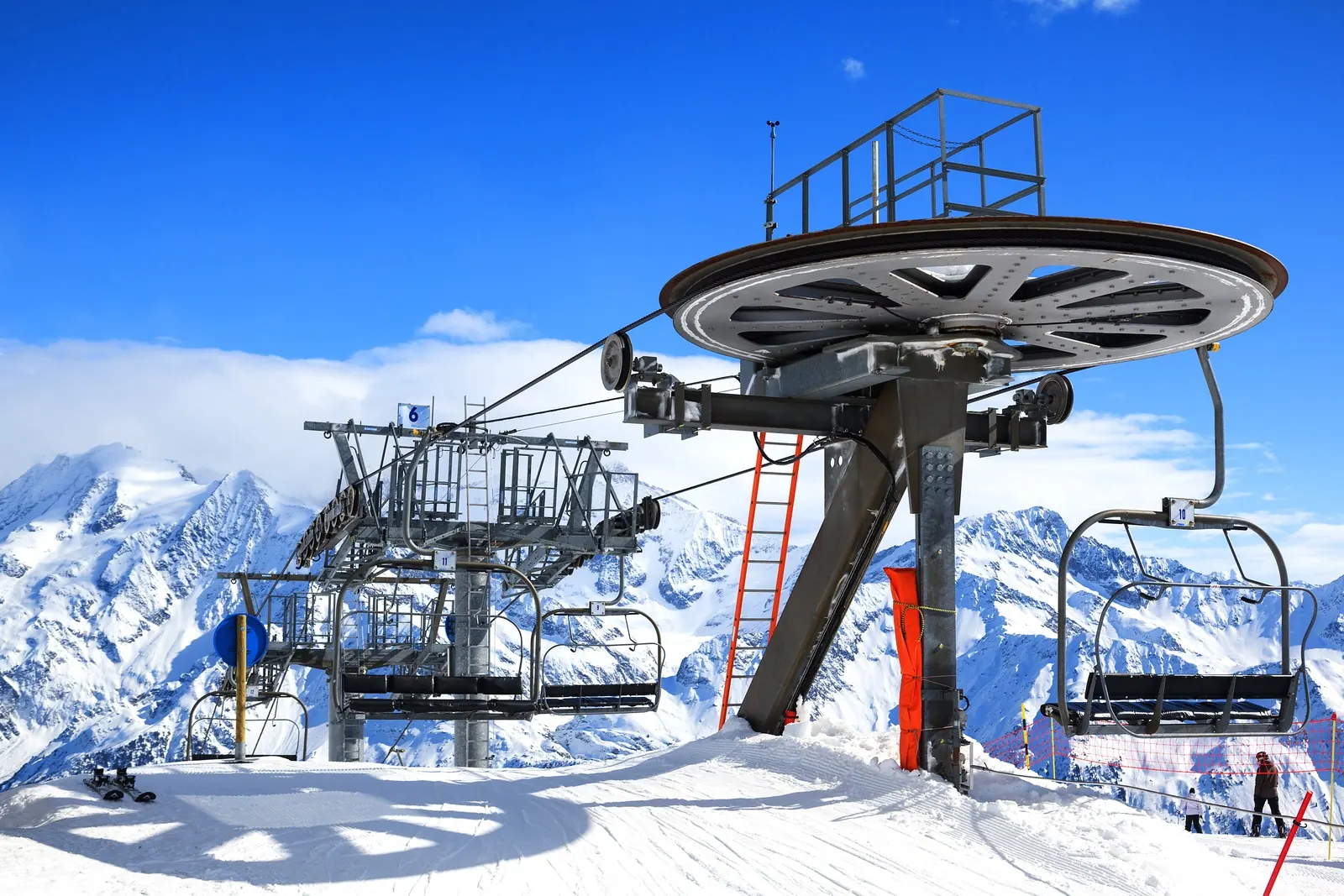 A chairlift station on a snowy summit with mountain peaks behind.