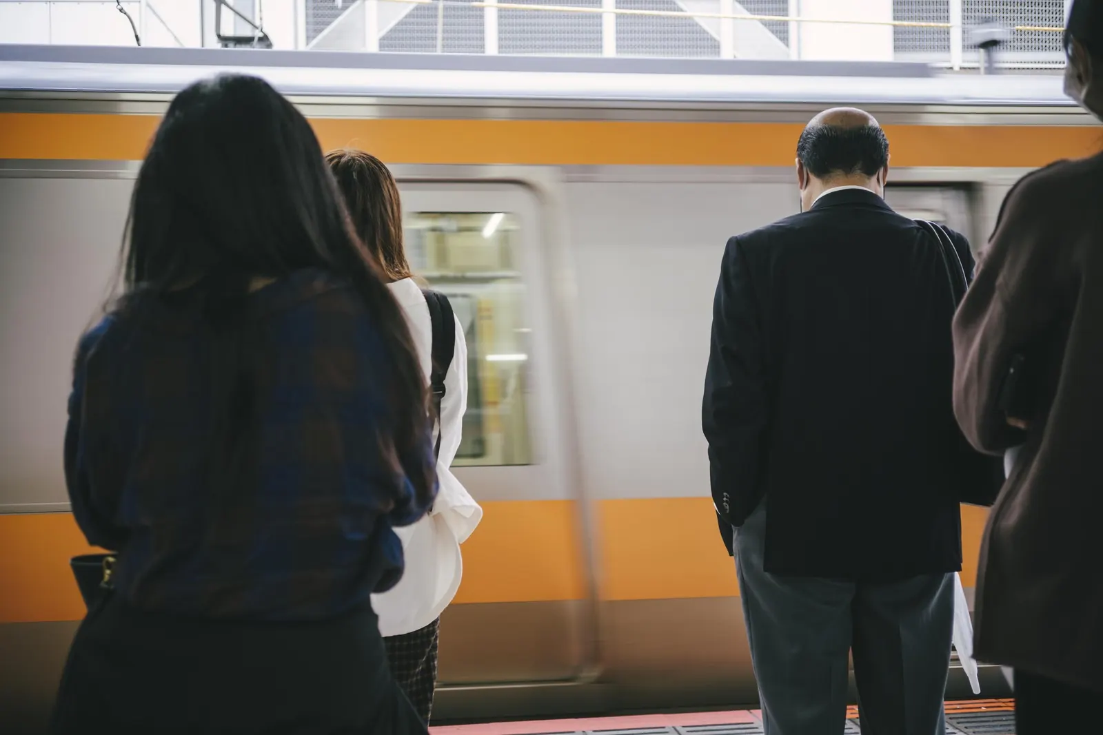 Passengers wait on a platform as a train arrives behind them.