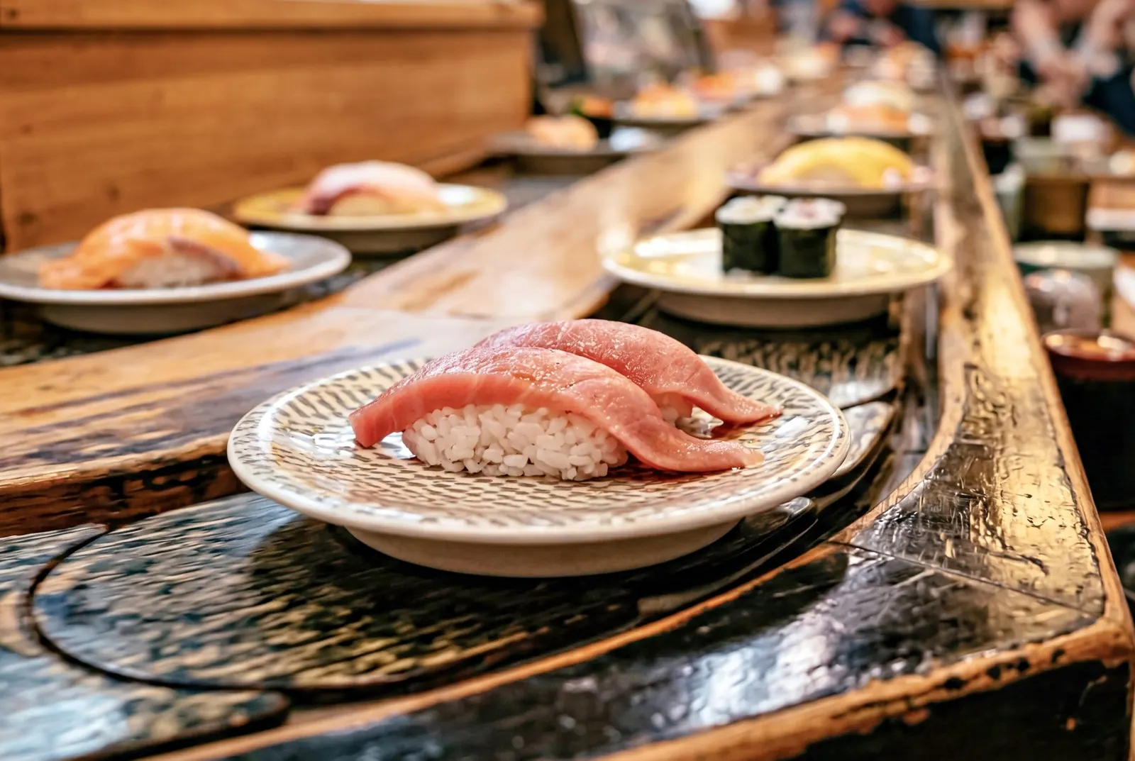 Plates of sushi passing on a conveyor belt: on the bus the lane runs past the upper-deck seats.
