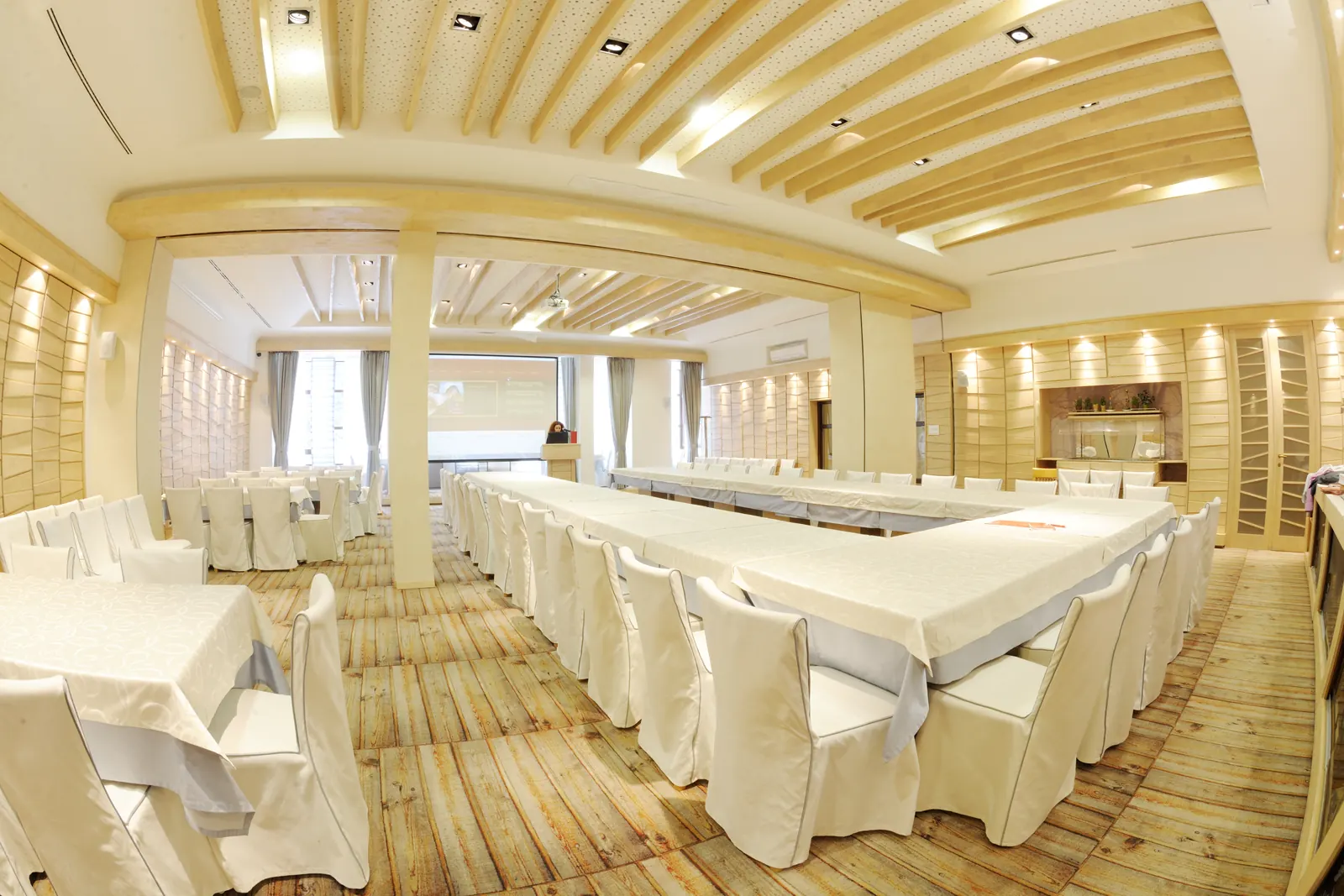 An empty meeting room with tables in a U-shape facing a screen.