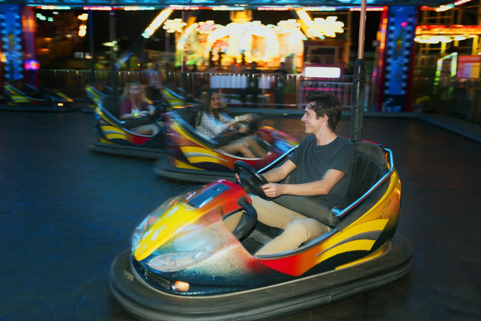 Friends ride bumper cars at an amusement park.