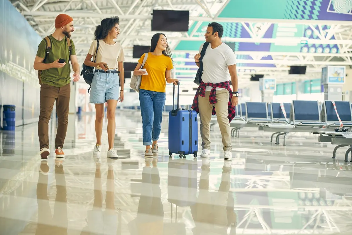 Four travellers with luggage walking through a bright terminal hall.