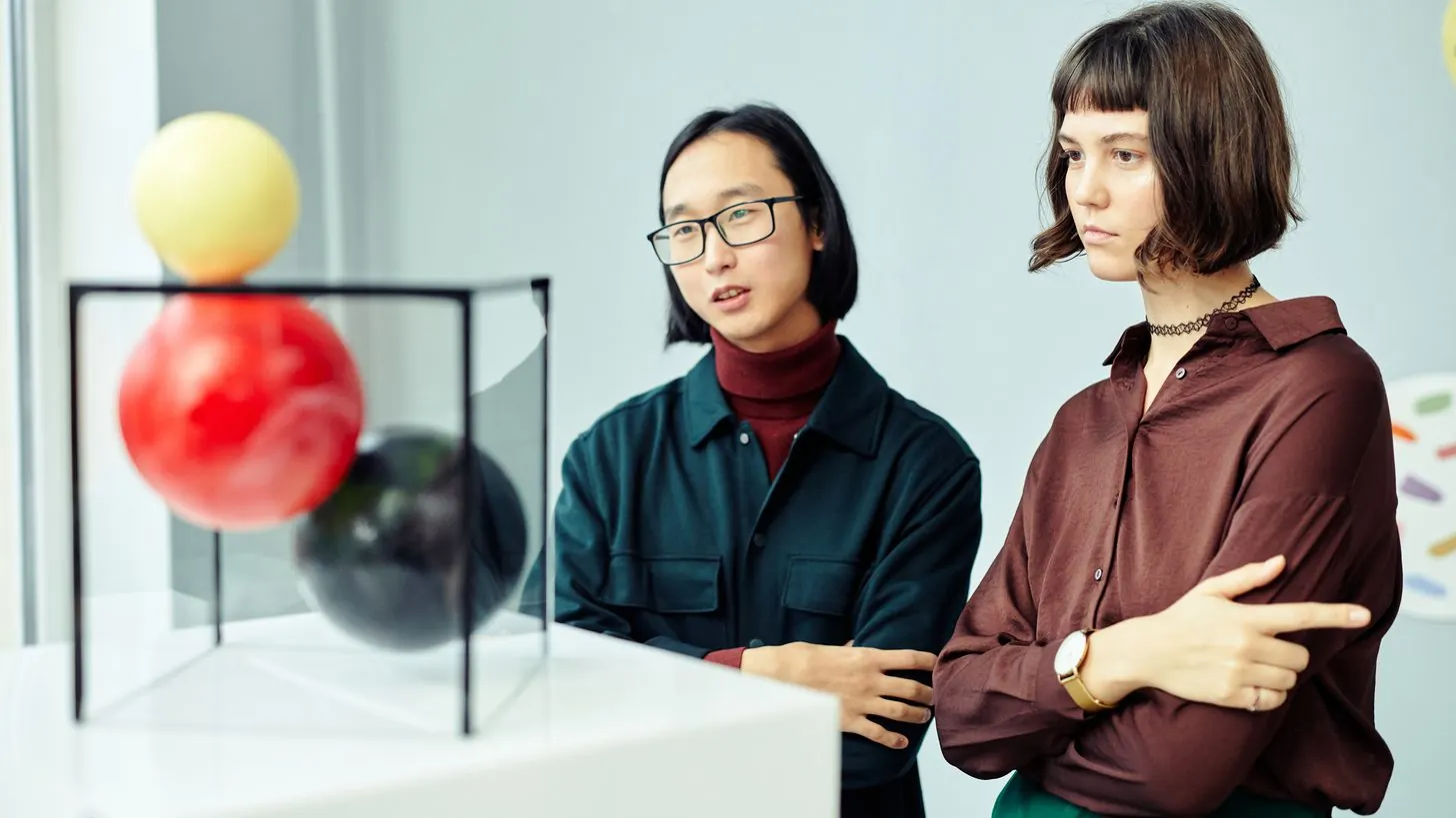 Two visitors looking at a sculpture in a bright gallery.