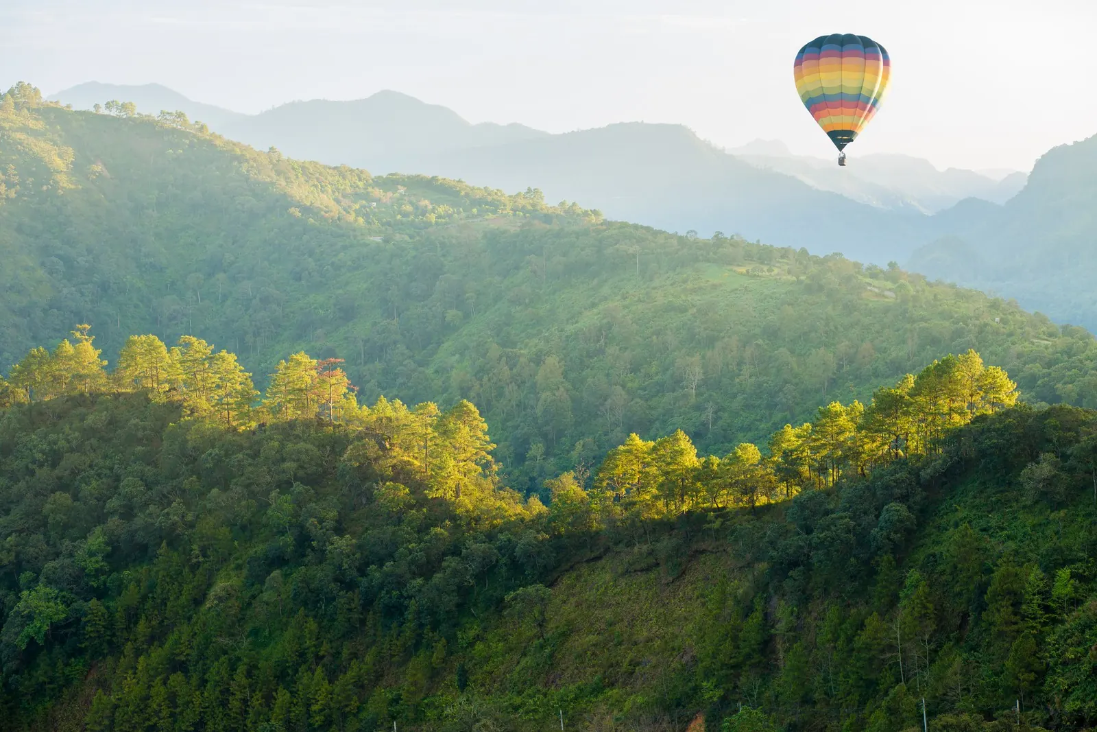 A hot air balloon floats above a green, forested mountain.