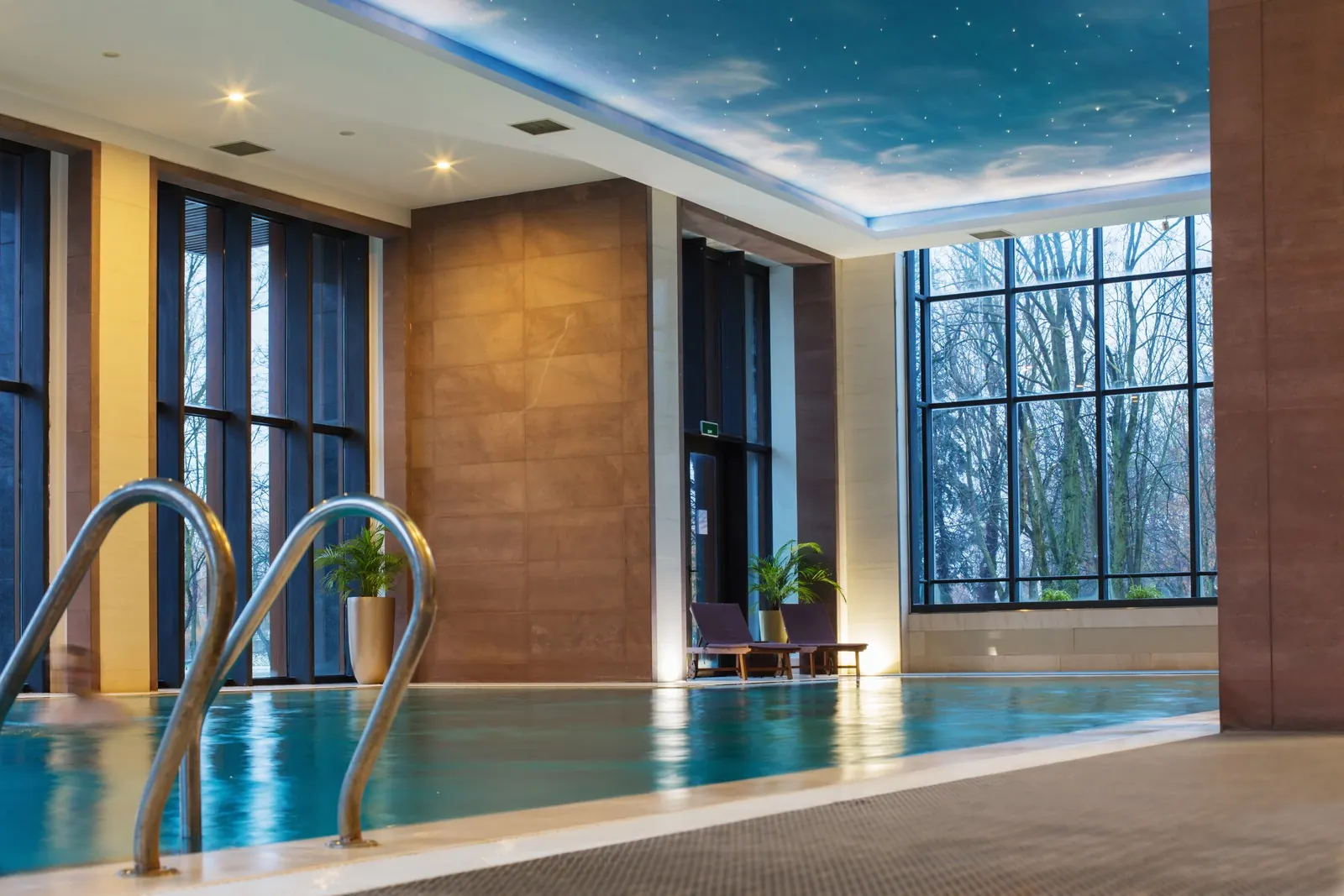 An indoor hotel swimming pool lit by large windows.