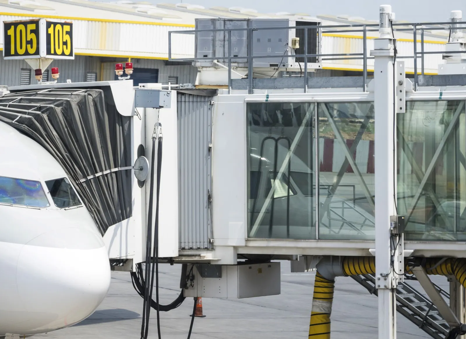 An airliner nose at a jet bridge beside a gate number sign.