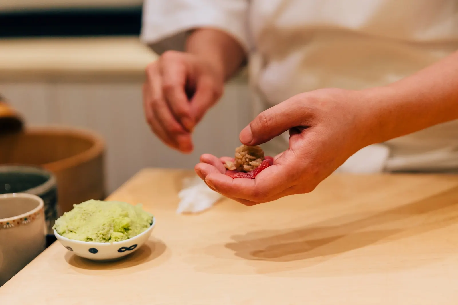 A sushi chef preparing nigiri at a wooden counter.