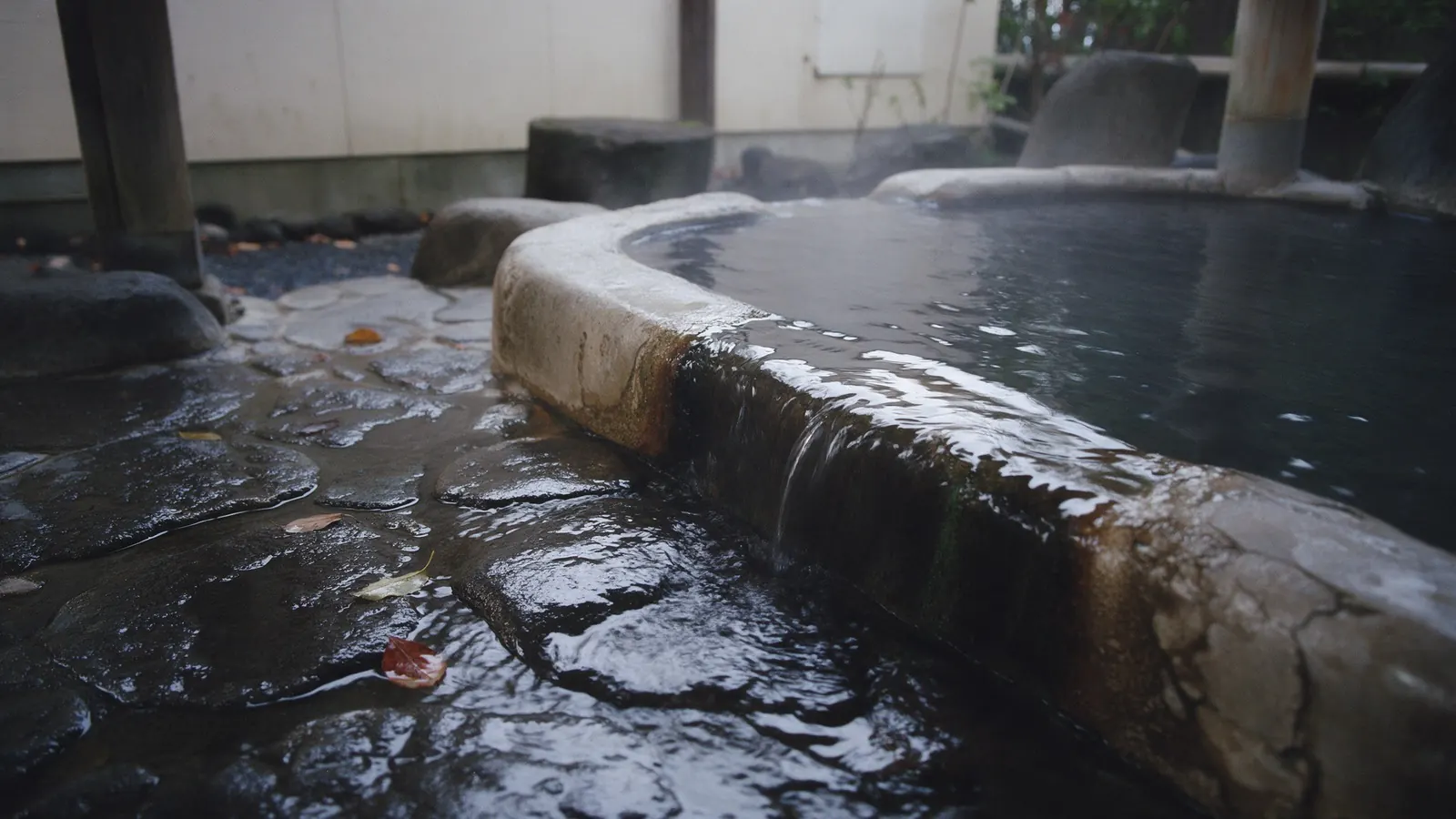Hot spring water spilling over the stone rim of a small outdoor bath.