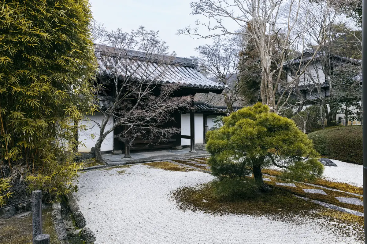 A raked gravel garden with a pine tree in front of a traditional building.