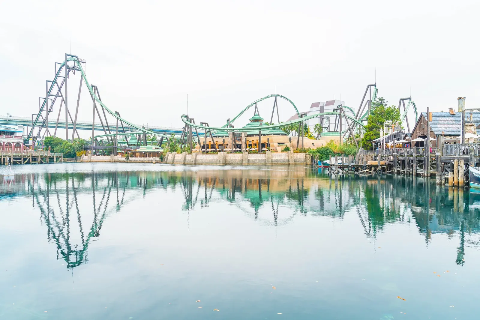 A roller coaster track curves above the water at a theme park.