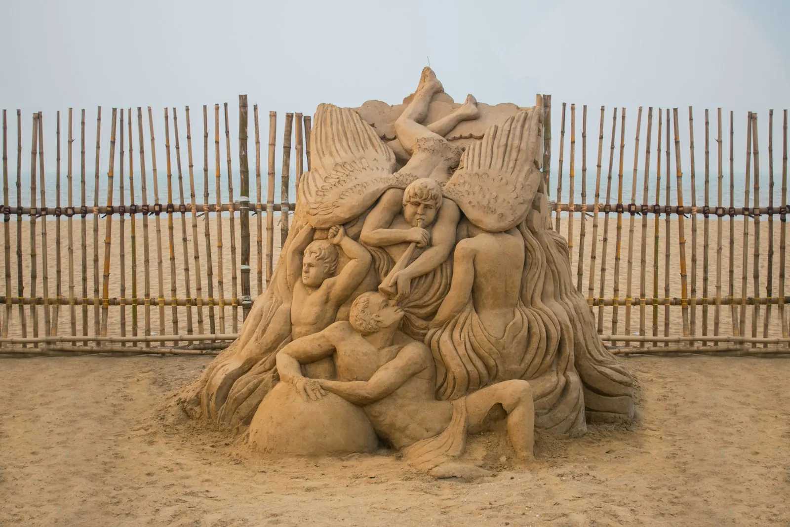 Sand sculptures of figures behind a beach fence: the exhibition is outdoors, so we plan for wind and rain.