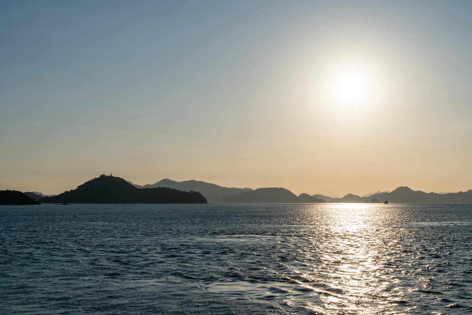 The sun low over a calm sea and a line of hilly islands.