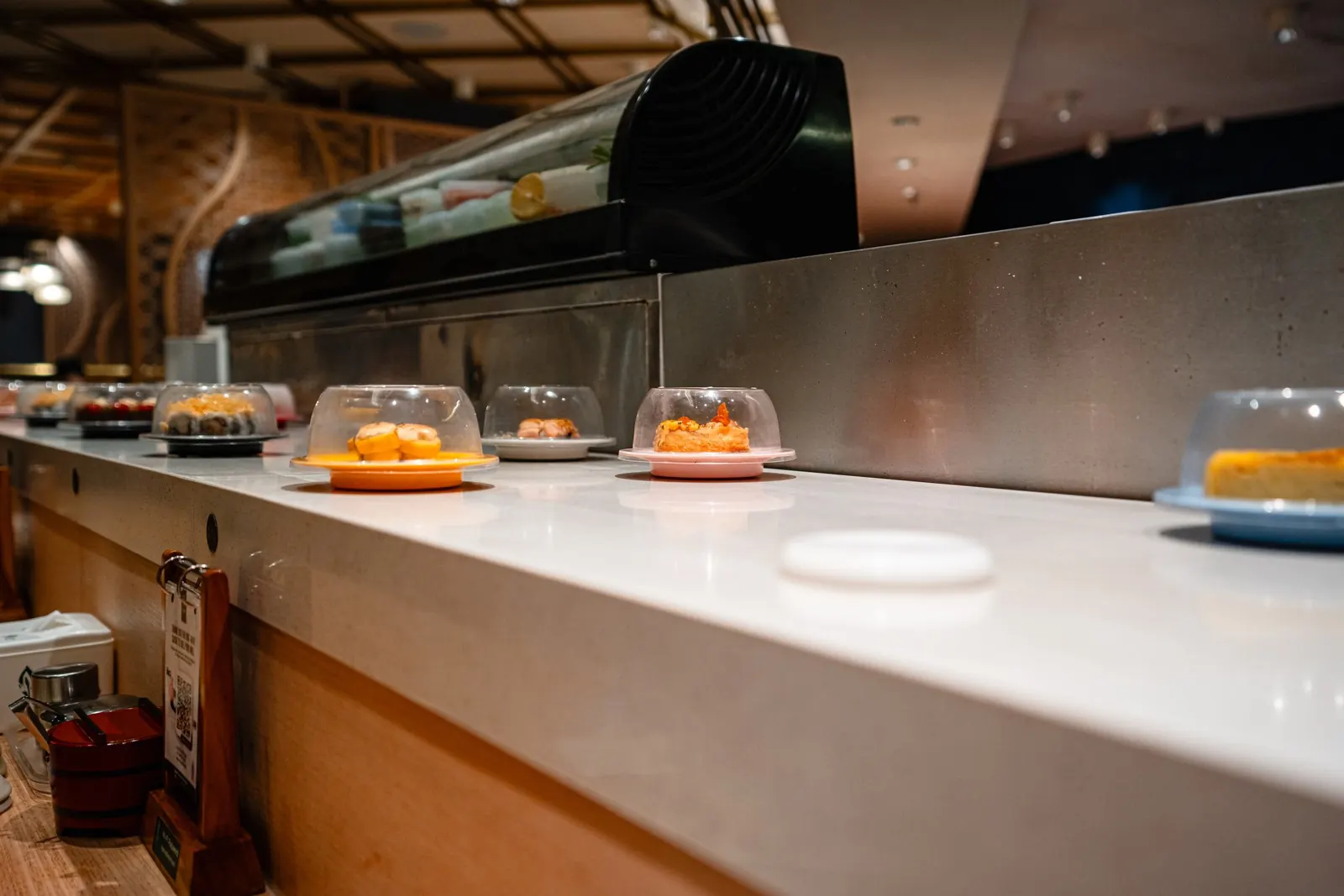 Covered sushi plates on a restaurant conveyor lane: we confirm dietary needs before booking.