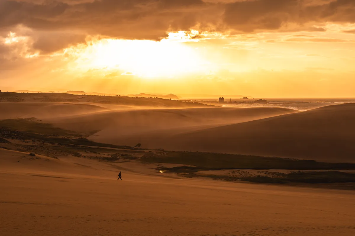Wind lifting sand over the Tottori Sand Dunes at sunset: covers for cameras and phones are worth packing.