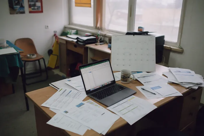 A wall calendar above a cluttered work table: bloom dates move with the weather, so the park day stays flexible.