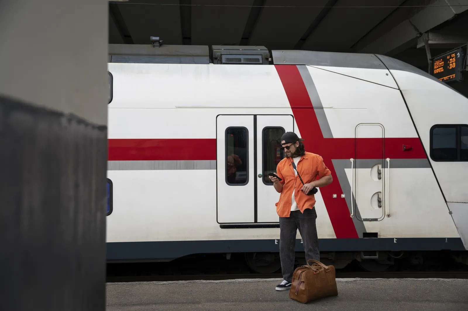 A traveller with a large bag stands beside a train on a platform.