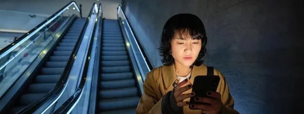 A traveller checking her phone beside an escalator: a digital pass only works while the phone does.