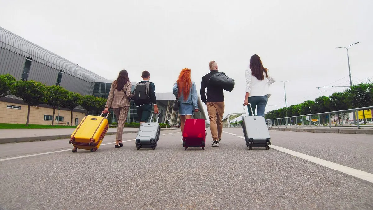 Five travellers pulling suitcases along a road outside a terminal.
