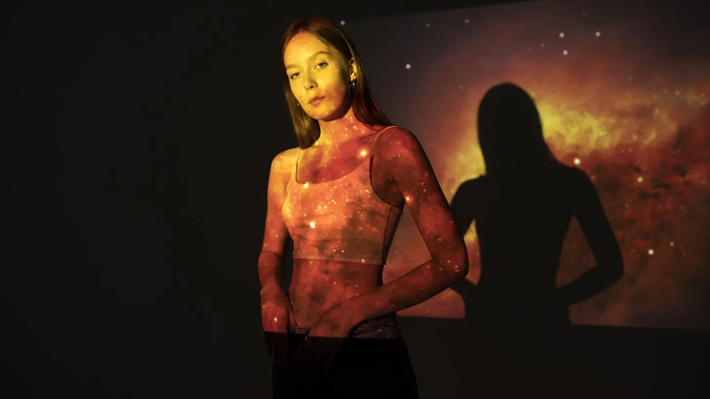 A visitor lit by a large projected image in a dark gallery.