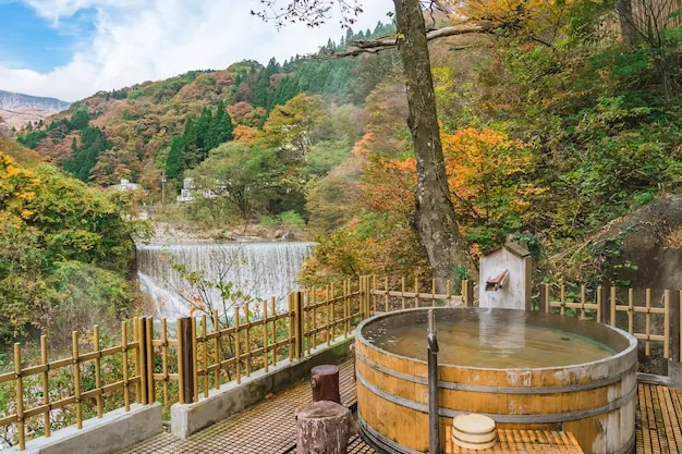 A wooden tub of hot spring water on a deck above an autumn valley.