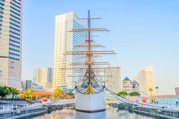A tall ship berthed below waterfront towers in Yokohama, one of Japan's main embarkation ports.